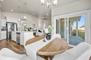 Dining area featuring hardwood / wood-style flooring, ceiling fan with notable chandelier, sink, and vaulted ceiling