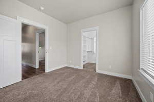 Unfurnished bedroom with a walk in closet, a closet, and dark carpet