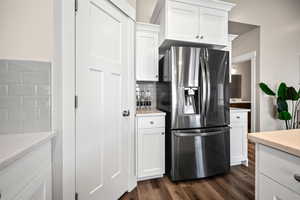 Kitchen with light stone countertops, stainless steel fridge, dark hardwood / wood-style flooring, decorative backsplash, and white cabinetry