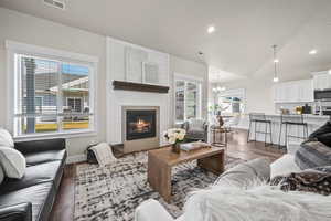 Living room with a large fireplace, an inviting chandelier, a wealth of natural light, and lofted ceiling