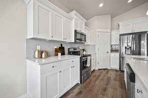 Kitchen with lofted ceiling, light stone counters, white cabinetry, and stainless steel appliances