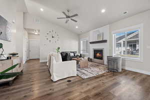 Living room featuring dark hardwood / wood-style flooring, a large fireplace, vaulted ceiling, and ceiling fan