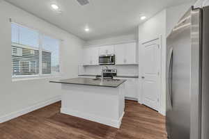 Kitchen with a kitchen island with sink, dark wood-type flooring, white cabinets, sink, and stainless steel appliances