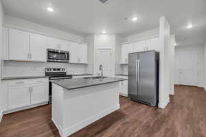 Kitchen featuring appliances with stainless steel finishes, tasteful backsplash, sink, a center island with sink, and white cabinetry