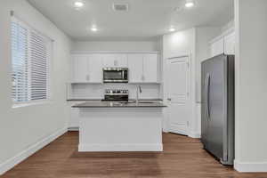 Kitchen with stainless steel appliances, white cabinetry, dark wood-type flooring, and an island with sink