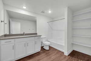 Full bathroom with hardwood / wood-style floors, a textured ceiling, toilet, shower / washtub combination, and vanity