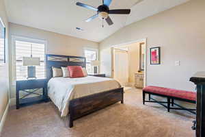 Bedroom with ensuite bathroom, ceiling fan, light colored carpet, and lofted ceiling