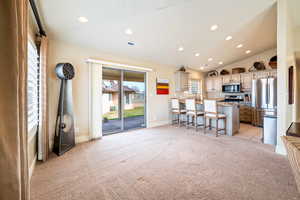 Kitchen featuring light carpet, stainless steel appliances, a breakfast bar area, a kitchen island, and lofted ceiling