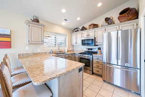 Kitchen with kitchen peninsula, appliances with stainless steel finishes, a breakfast bar, sink, and light tile patterned flooring