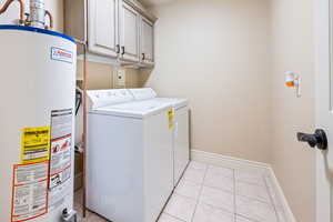 Laundry room featuring water heater, light tile patterned flooring, cabinets, and independent washer and dryer