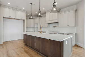 Kitchen featuring white cabinetry, a center island with sink, pendant lighting, and light wood-type flooring