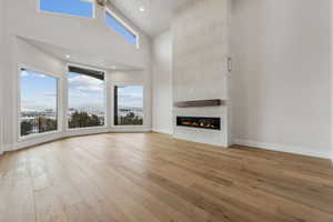 Unfurnished living room with beam ceiling, a large fireplace, high vaulted ceiling, and light hardwood / wood-style floors