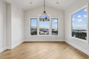 Unfurnished dining area with a notable chandelier, light hardwood / wood-style floors, and vaulted ceiling