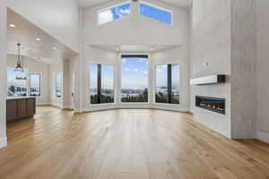 Family room featuring Bay window area, a fireplace, a high ceiling, light wood-type flooring, and a healthy amount of sunlight