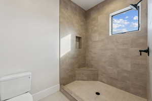 Bathroom featuring tiled shower, tile patterned floors, and toilet