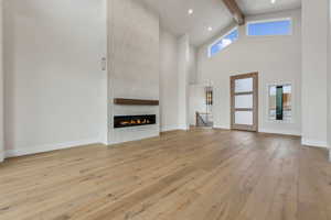 Unfurnished living room featuring a fireplace, a towering ceiling, beamed ceiling, and light wood-type flooring