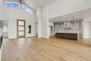 Unfurnished living room featuring sink, a high ceiling, and light hardwood / wood-style flooring