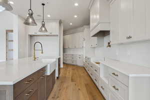 Kitchen with white cabinetry, sink, hanging light fixtures, an island with sink, and light hardwood / wood-style floors