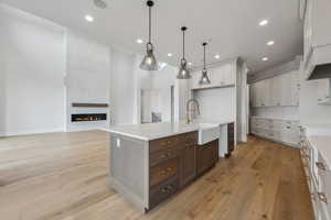 Kitchen featuring a large fireplace, a kitchen island with sink, sink, light hardwood / wood-style floors, and hanging light fixtures