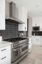 Kitchen featuring white cabinets, appliances with stainless steel finishes, tasteful backsplash, and wall chimney exhaust hood