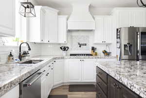 Kitchen featuring white cabinets, stainless steel appliances, premium range hood, and sink