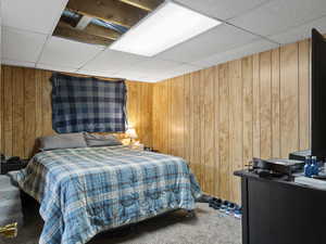 Carpeted bedroom with a paneled ceiling and wooden walls