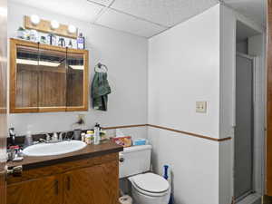 Bathroom featuring a drop ceiling, vanity, an enclosed shower, and toilet