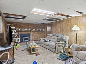 Carpeted living room featuring a paneled ceiling, a wood stove, and wooden walls