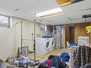 Laundry area with heating unit, light tile patterned flooring, wooden walls, and washing machine and clothes dryer