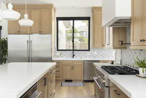 Kitchen with sink, pendant lighting, high quality appliances, light brown cabinetry, and custom range hood