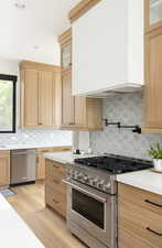 Kitchen with stainless steel appliances, backsplash, light hardwood / wood-style floors, light brown cabinetry, and custom range hood