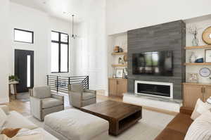 Living room with a fireplace, a towering ceiling, light wood-type flooring, and a notable chandelier