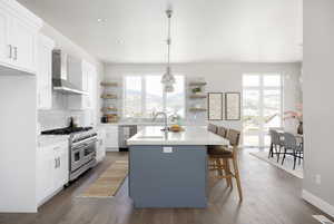 Kitchen featuring wall chimney exhaust hood, stainless steel appliances, plenty of natural light, an island with sink, and pendant lighting