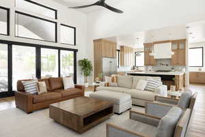 Living room featuring ceiling fan, a towering ceiling, and light wood-type flooring