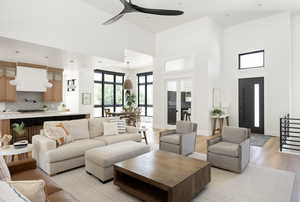 Living room with ceiling fan, a towering ceiling, and light hardwood / wood-style flooring