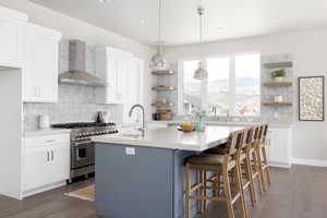 Kitchen with wall chimney exhaust hood, a mountain view, double oven range, a kitchen island with sink, and white cabinets