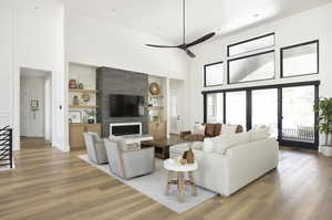 Living room with built in shelves, ceiling fan, a fireplace, and a towering ceiling