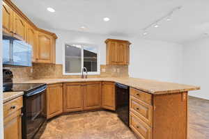 Kitchen featuring kitchen peninsula, decorative backsplash, rail lighting, sink, and black appliances