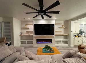 Living room featuring a fireplace, ceiling fan, light wood-type flooring, and a textured ceiling