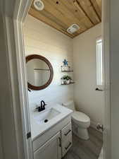 Bathroom with vanity, wood walls, wooden ceiling, hardwood / wood-style flooring, and toilet