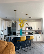 Kitchen featuring hanging light fixtures, light hardwood / wood-style floors, a breakfast bar, white cabinets, and appliances with stainless steel finishes