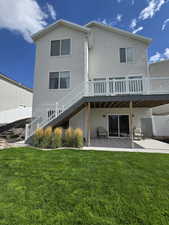 Back of house featuring a wooden deck, a patio area, and a lawn