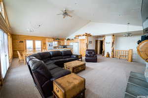 Living room with carpet flooring, log walls, lofted ceiling, wooden walls, and ceiling fan with notable chandelier