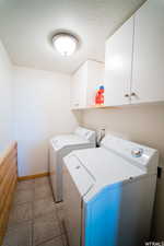 Laundry area featuring tile patterned floors, cabinets, a textured ceiling, and washing machine and clothes dryer