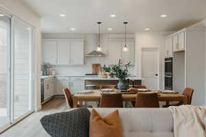 Kitchen with white cabinetry, hanging light fixtures, light wood-type flooring, decorative backsplash, and wall chimney range hood