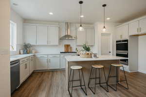 Kitchen featuring hanging light fixtures, appliances with stainless steel finishes, wall chimney range hood, and white cabinets