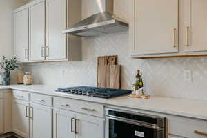 Kitchen featuring tasteful backsplash, white cabinets, wall chimney exhaust hood, and appliances with stainless steel finishes