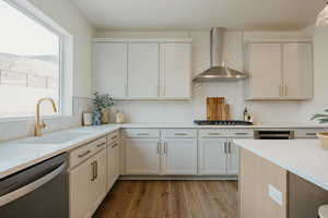 Kitchen featuring sink, appliances with stainless steel finishes, white cabinetry, light hardwood / wood-style floors, and wall chimney exhaust hood