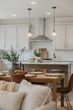 Kitchen featuring a kitchen bar, white cabinetry, tasteful backsplash, decorative light fixtures, and wall chimney range hood