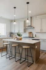 Kitchen featuring wall chimney exhaust hood, a breakfast bar area, a center island, hanging light fixtures, and white cabinets